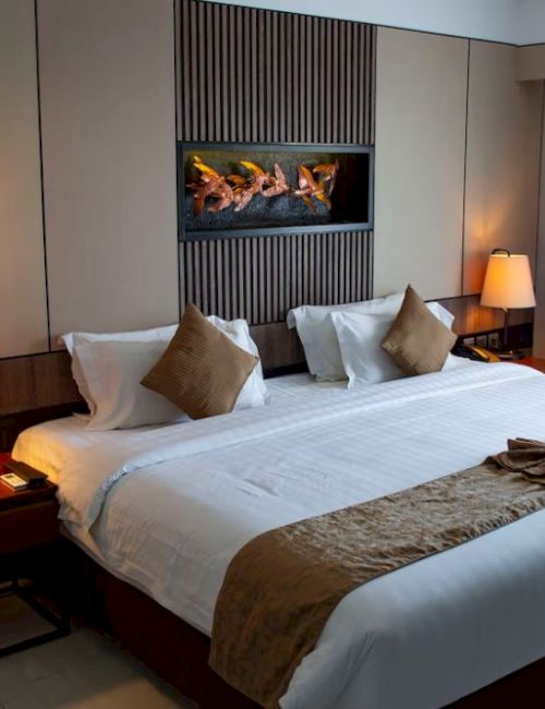 A cozy hotel room with a large bed, pillows, side tables with lamps, a decorative wall panel, and curtains over a window, creating a warm ambiance.
