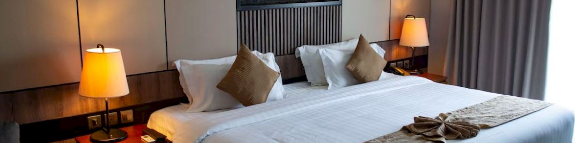 A neatly arranged hotel room with a large bed, two bedside tables with lamps, and wall art above the headboard, and a curtain on the right.