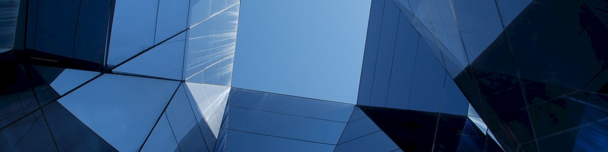 The image features a view looking up through a geometric arrangement of reflective glass panels with a blue sky visible at the center.