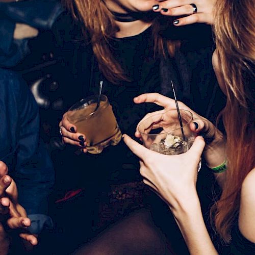 Three people in a dimly lit setting, holding drinks and engaging in conversation, with visible smiles and laughter.