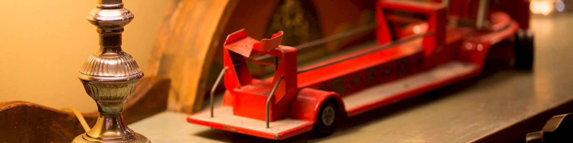 This image shows a metallic table lamp, a vintage red toy fire truck, and a circular wooden decor piece on a surface.