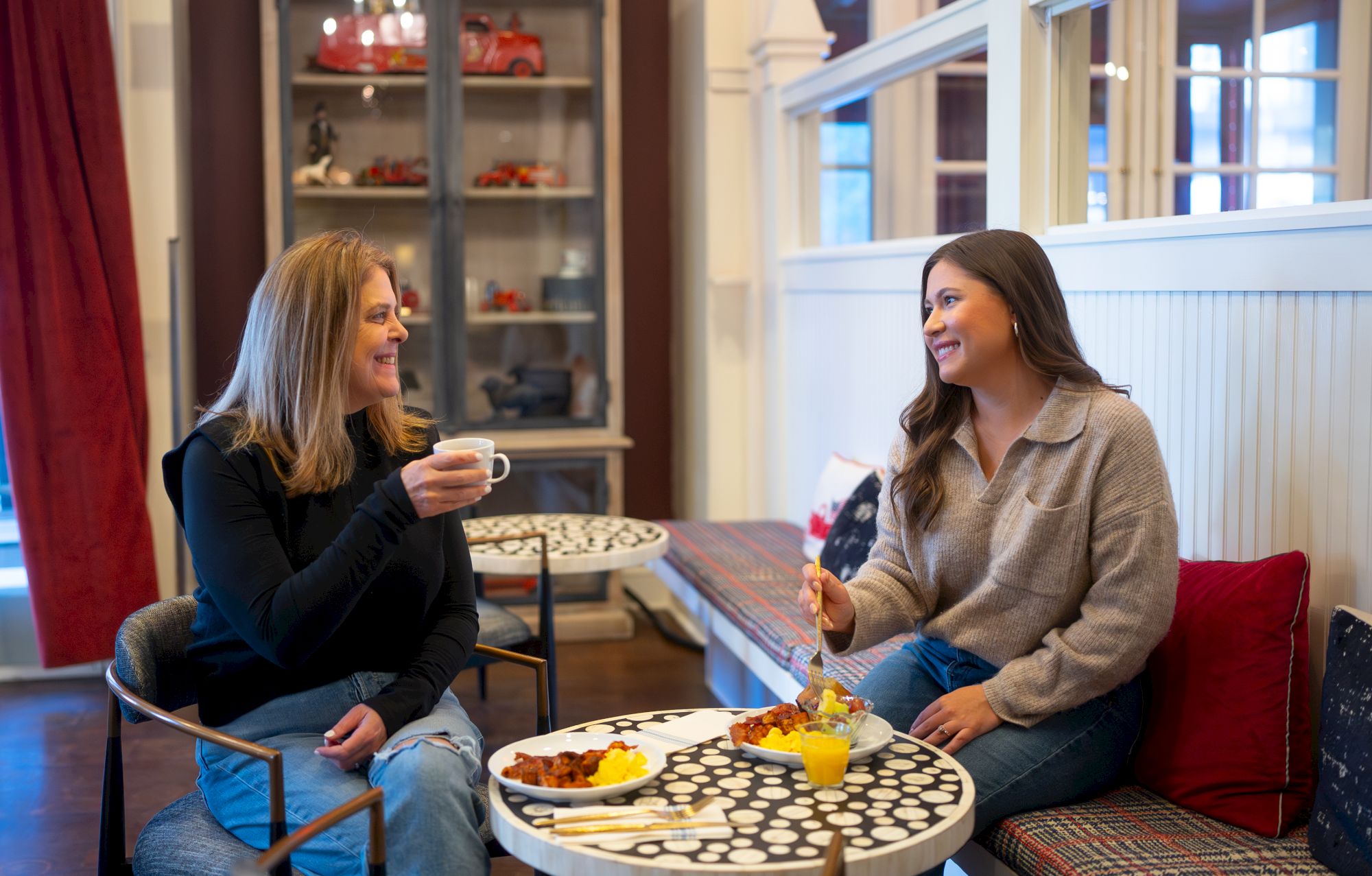 Two women are seated at a table, enjoying breakfast and engaging in a pleasant conversation indoors.