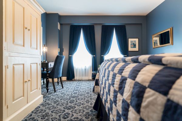 A room with blue-checkered bedding, dark blue curtains, a desk with a lamp, a chair, and beige storage cabinets against a blue wall ends the sentence.