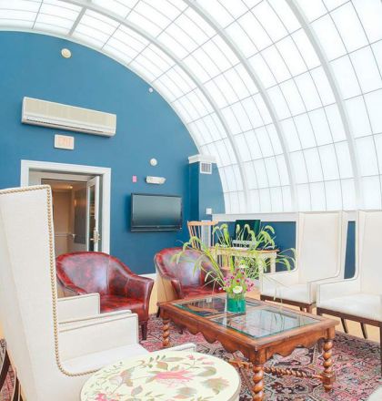 A bright room with a curved glass ceiling features eclectic seating, a TV, plants, and a mix of contemporary and vintage furniture and décor.