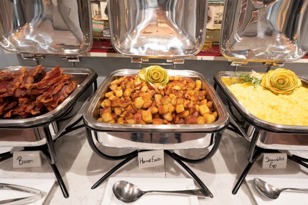 This image shows a buffet with containers labeled bacon, home fries, and scrambled eggs, each topped with a decorative garnish.