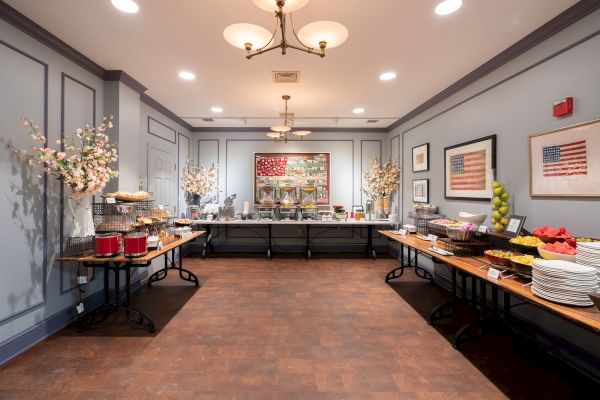 A well-decorated room with a buffet setup featuring a variety of food items and drinks on tables, surrounded by framed art on the walls.