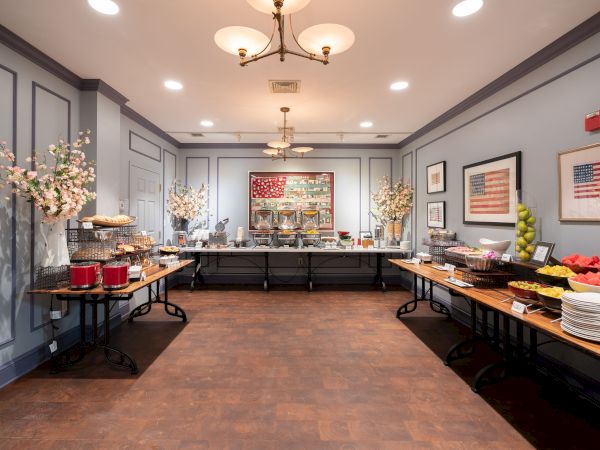 A well-decorated room with a buffet setup featuring a variety of food items and drinks on tables, surrounded by framed art on the walls.