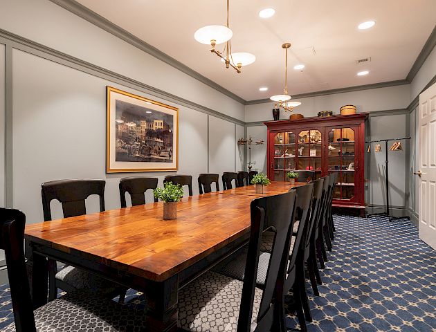 This is an image of a dining room with a long wooden table, black chairs, and a red cabinet. The room is well-lit with ceiling lights.