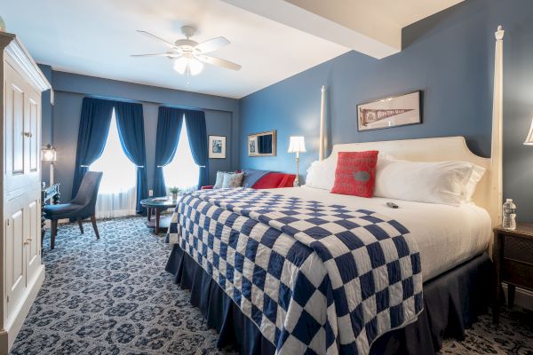 A cozy bedroom features a large bed with a blue and white checkered quilt, elegant curtains, and stylish decor in a soothing blue color scheme.