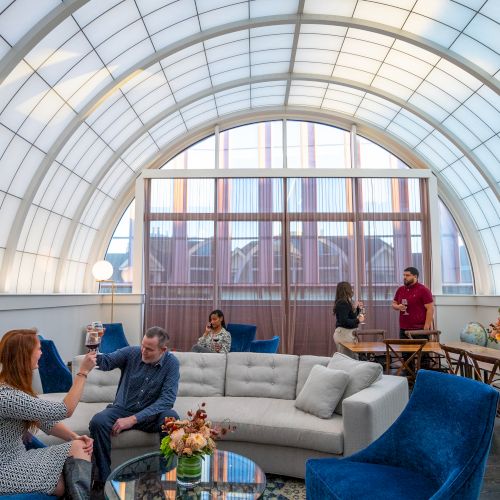 A group of people socializing in a stylish rooftop with blue and white chairs, and a decorative flowers display.