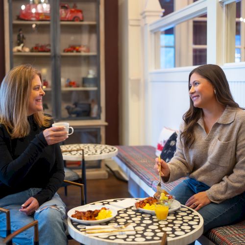 Two women enjoying a meal and drinks at a cozy cafe, smiling and chatting.