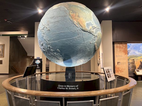 A large globe display in a museum setting, labeled "Given in Memory of Charles W. Brown, Jr." with information panels around it, ending the sentence.