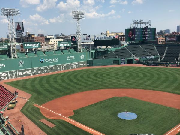 A view of an empty baseball stadium with a green field and batting practice setup in the infield. Stadium seats and lighting towers are visible.