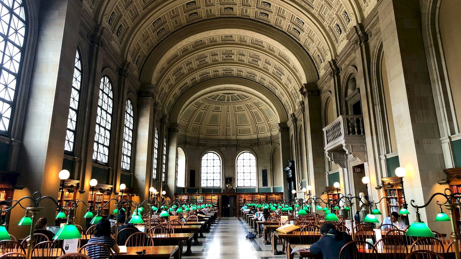 The image shows the interior of a large, historic library with high arches, rows of long tables, and green desk lamps, ending the sentence.