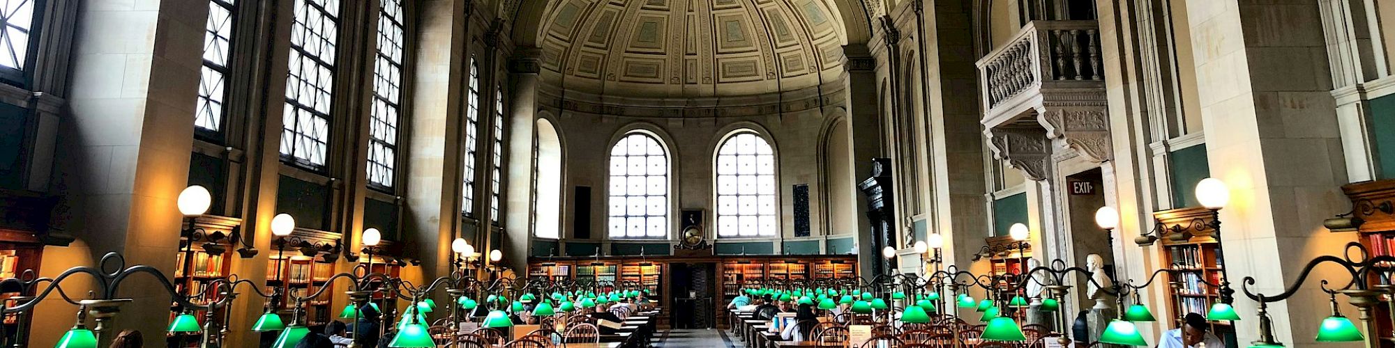 The image shows the interior of a large, historic library with high arches, rows of long tables, and green desk lamps, ending the sentence.