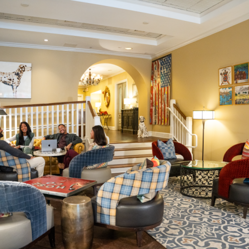 A cozy lounge with people gathered, colorful chairs, wall art, and soft lighting in a warm, inviting setting.