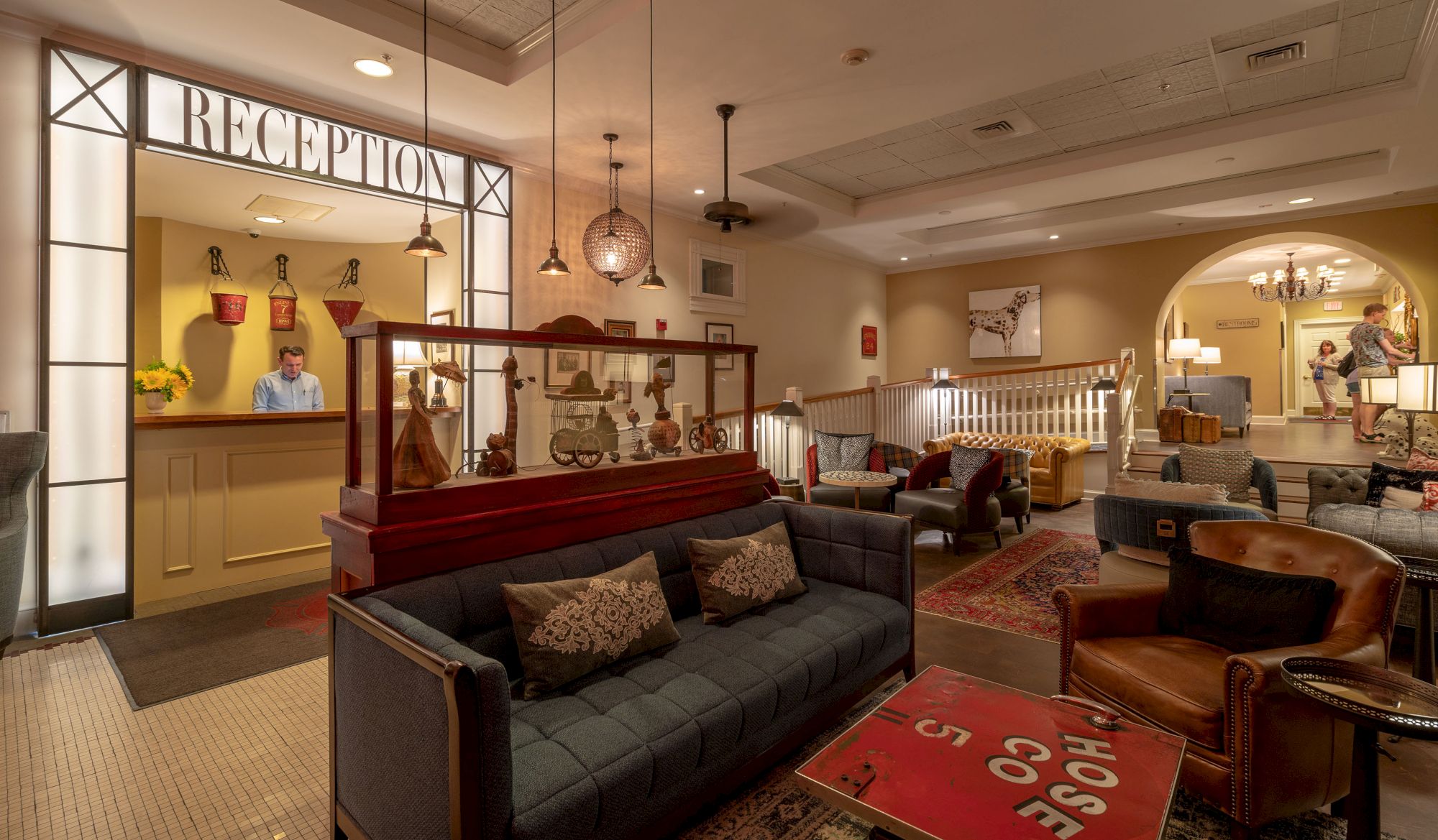 This image shows a reception area with a person at the desk, a cozy seating area with sofas and chairs, and eclectic decor throughout the space.