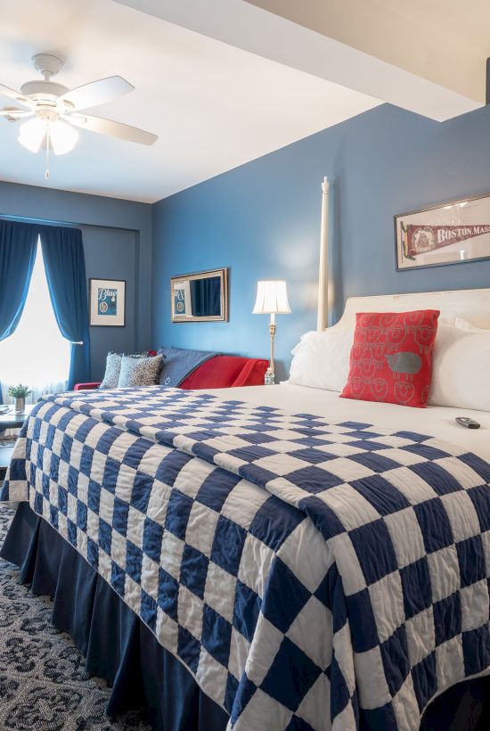 A cozy bedroom with a large bed, blue and white decor, patterned carpet, and a ceiling fan, creating a welcoming ambiance.