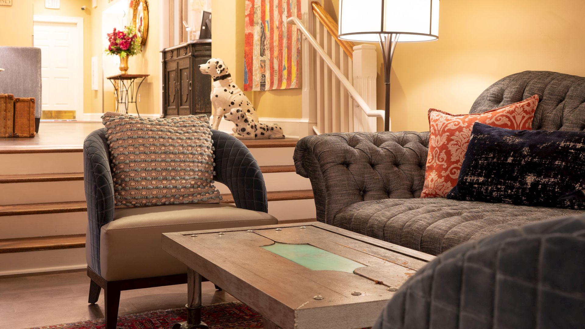 A cozy living room with a gray sofa, armchair, rustic coffee table, and a decorative Dalmatian statue by the staircase ending the sentence.