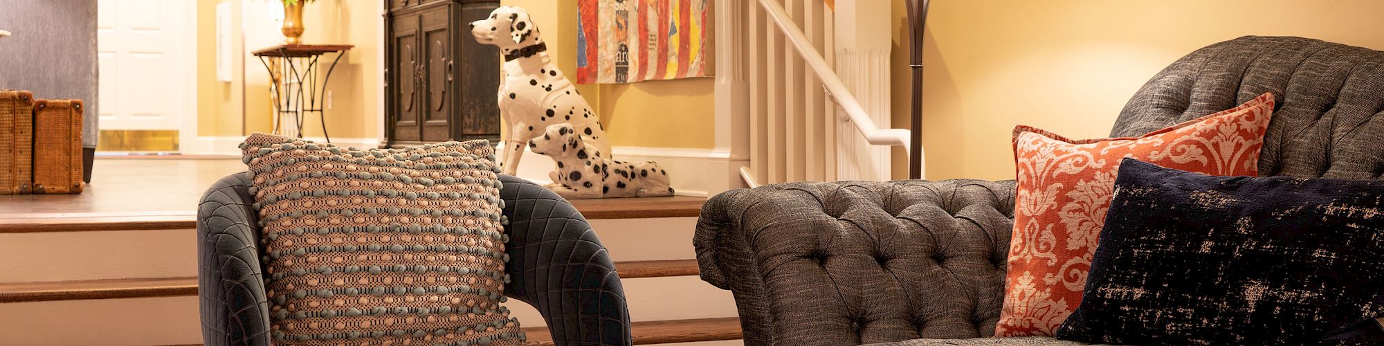 A cozy living room with a gray sofa, armchair, rustic coffee table, and a decorative Dalmatian statue by the staircase ending the sentence.