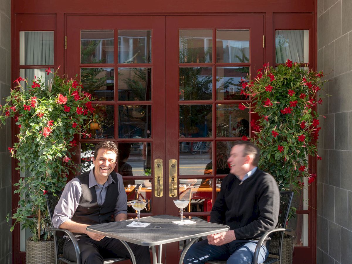 Two people sitting at an outdoor table of a restaurant with a red "RESTAURANT" sign above the door, enjoying drinks and chatting.