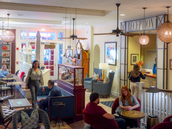 A cozy hotel lobby with people sitting, a reception desk, and shelves with decorations. A mix of seating and warm lighting enhances the space.