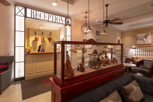 A hotel reception area with a receptionist, decorative items in a display case, comfortable seating, and warm lighting creates a welcoming ambiance.