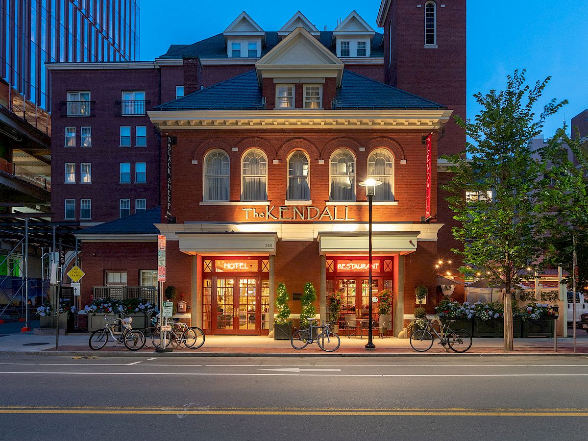 A charming, historic red-brick building with large windows and a small tower, set against a clear evening sky on a quiet street.
