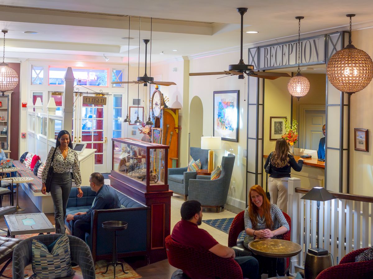 People in a cozy reception area; some are seated, one is at reception, and others are walking. The ambiance is warm and inviting.