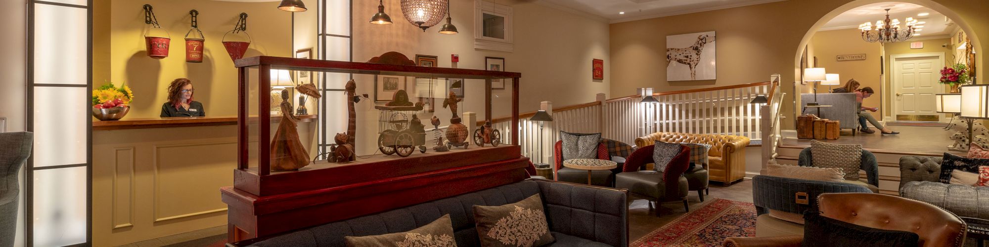 A cozy hotel lobby with vintage decor, featuring a reception desk, sofas, chairs, and lamps, creating a welcoming atmosphere.