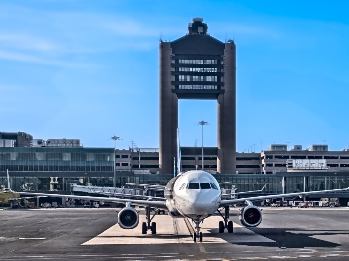 A passenger plane on the runway with a modern control tower in the background, under a clear blue sky.