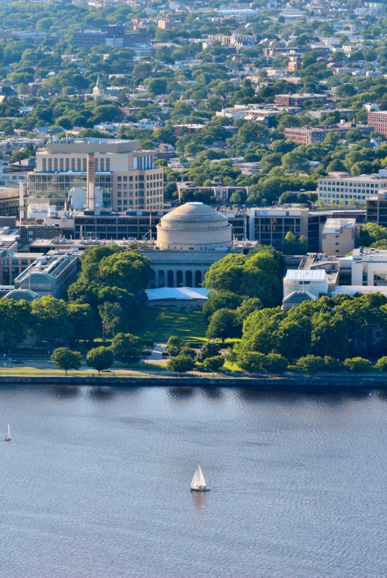 An aerial view of a city with a prominent domed building near a river, surrounded by greenery and smaller structures.
