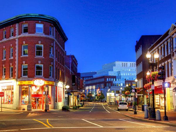 A vibrant city street at dusk with historic buildings, lit storefronts, and streetlights creating a warm ambiance.