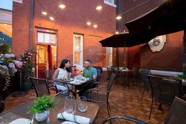 A couple is dining outdoors at a restaurant patio in the evening, with string lights and a cozy ambiance surrounding them.