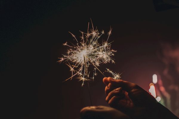 A hand holding a lit sparkler against a dark background, creating a festive and bright display.