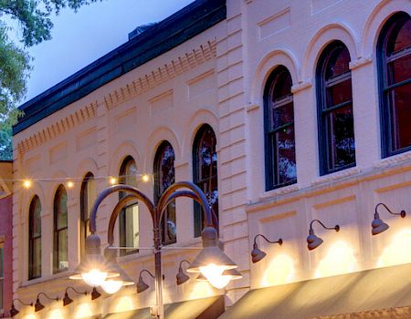 Charming streetscape with historic brick buildings, arched windows, and decorative lights under a large tree.
