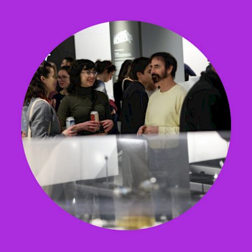 People are gathered at an event or exhibition, with some holding drinks, set against a purple circular frame.