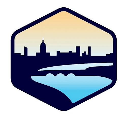 The image depicts a logo with a city skyline, river, and bridge inside a hexagonal shape against a gradient sky background.