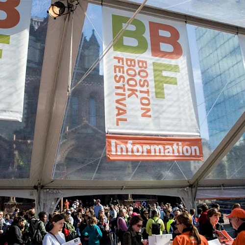 A large crowd gathers under a tent with banners for the Boston Book Festival, alongside an Information sign, in an outdoor setting.