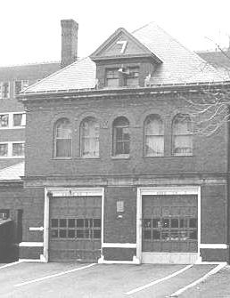 A two-story brick building with three garage-style doors on the ground floor, arched windows on the upper floor, and a small peaked dormer on the roof.