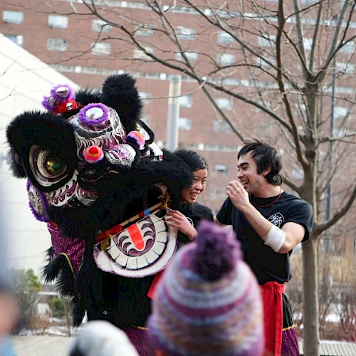 A man watches a colorful dragon dance in an outdoor urban setting.
