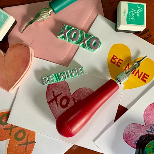 Colorful craft scene with heart stickers, stampers, and brushes on papers; messages like BE MINE and XO appear; playful handmade cards inside.