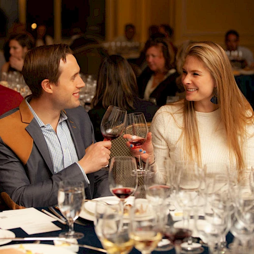 Two people at a restaurant toasting with wine glasses, smiling and enjoying a dinner together.