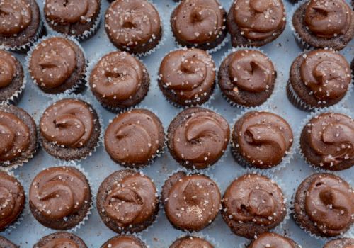 Delicious chocolate truffle cupcakes arranged in neat rows on a cooling rack, glossy swirled tops and tiny sugar crystals sprinkled on.