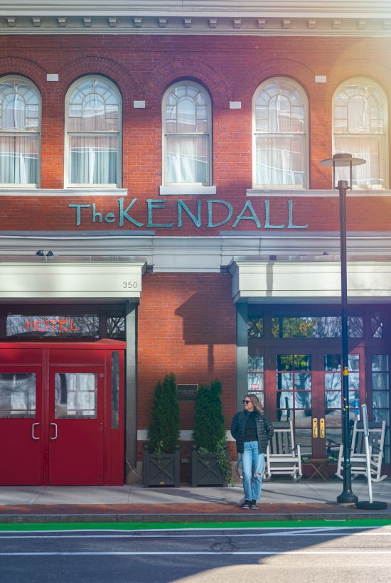 A person walks past The Kendal building with storefronts, red doors, and colorful windows.