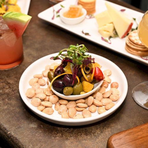 A small plate with a stacked, herb-topped bite, alongside a skewer and a red sauce in a glass, on a rustic wooden table.