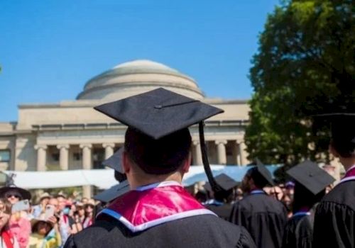 Graduation ceremony outdoors with graduates in caps and gowns, a domed building in the background, and a crowd watching. End.