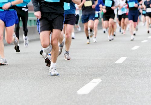 A group of runners racing on a wide road, wearing colorful athletic gear and numbered bibs, moving fast in a marathon-style event.