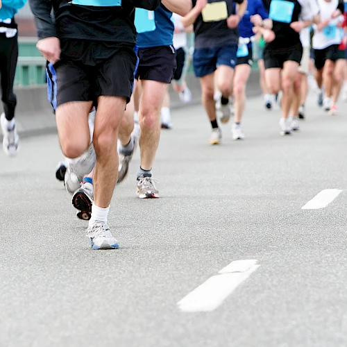 A group of runners racing on a wide road, wearing colorful athletic gear and numbered bibs, moving fast in a marathon-style event.
