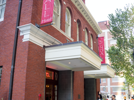 A brick theater building with pink banners reading &ldquo;KINDAI&rdquo; (likely the Kindra? theater) advertising a show, people walking outside, sunny day.